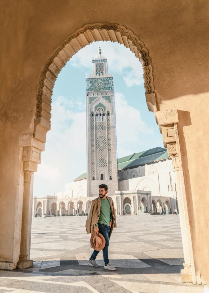 Man walking through archway with Hassan II Mosque minaret in Casablanca, Morocco.